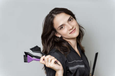 close-up photo of beautiful young woman hairdresser. stylist holds scissors, professional brushes and a comb in his hands and smiles. layout for design. beauty salon concept.の写真素材