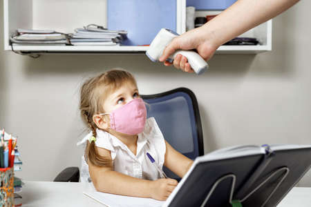 measuring body temperature of a girl in a protective maskの写真素材