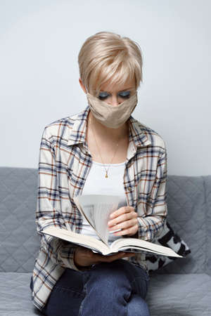 young blonde woman in protective mask reading a book. self-isolation due to covid-19の写真素材