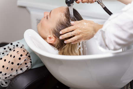 hair stylist washing hair of yong blonde young woman in hair salon before haircutの写真素材