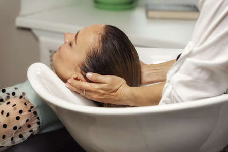 Beauty salon beautiful woman getting hair wash in white sink.の写真素材