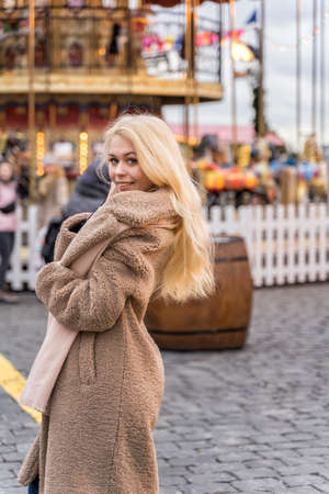 01 14 2020 Moscow, Russian Federation, beautiful young woman in a light fur coat made of faux fur stands at the Christmas carousel and smiles.のeditorial素材