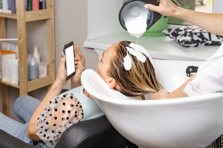 woman in a beauty salon. hair care. hairdresser applies mask to client's hair. the female is looking...