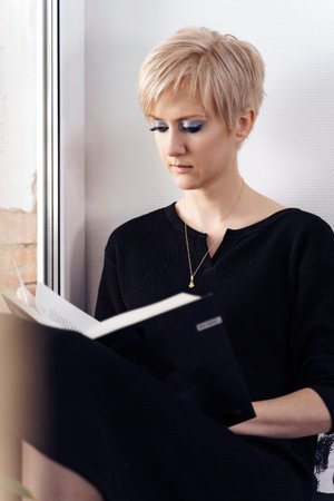 young woman reading a book by the windowの写真素材