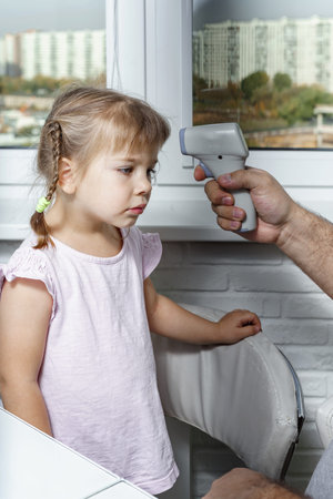 Close up of dad hand checking temperature of her sick daughter by electronic medical infrared...