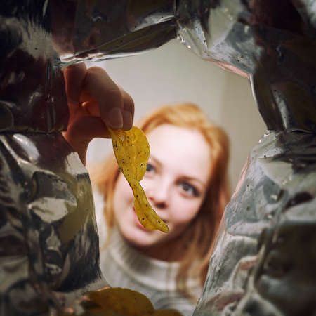 a sweet girl with appetite takes out chips from a pack. view from the packの写真素材