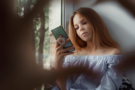 girl sits by the window and uses a smartphone. terrible hands threaten to seize the woman. social...