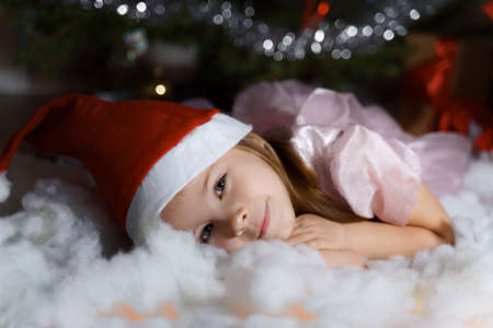 a child in a santa hat lies by the tree and dreams. christmas and new year conceptの写真素材