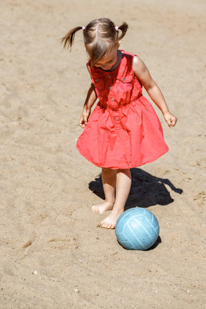 cute little girl in a red dress plays with a ball on the sand. summer vacation conceptの写真素材