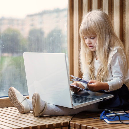 blonde girl holding euro bills in hands. child uses laptop. Finance and success business concept.の写真素材