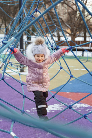 portrait of a cute caucasian girl in winter clothes on a walk in the playgroundの写真素材