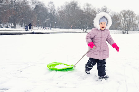 cute little girl in winter clothes runs in the snow with a sled. the winter vacationの写真素材