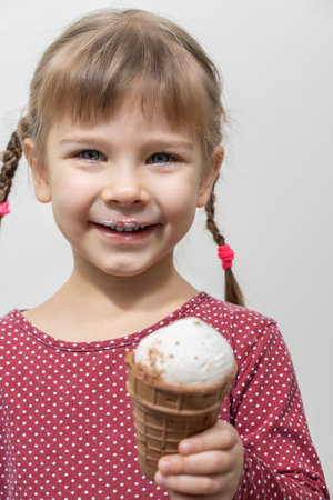 happy little caucasian girl in a red dress eating ice cream and smileの写真素材