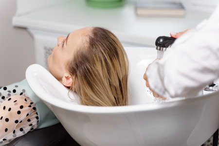 Beautiful blond woman getting hair wash in beauty salon. Concept head treatment care.の写真素材