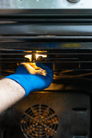 The hand of a man in blue gloves changes the light bulb in the oven