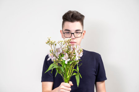 serious young man in glasses with a bouquet of white flowers on a gray backgroundの写真素材