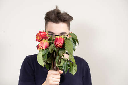 young guy in glasses with a bouquet of withered red roses. unhappy love conceptの写真素材