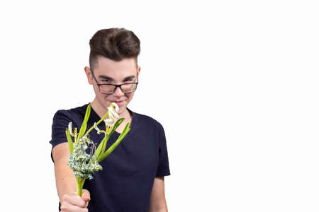 a malicious young man with glasses holds out a bouquet of wilted flowers and smiles. the concept of greed and stinginess. focus on flowers, guy in blur. isolate, white backgroundの写真素材