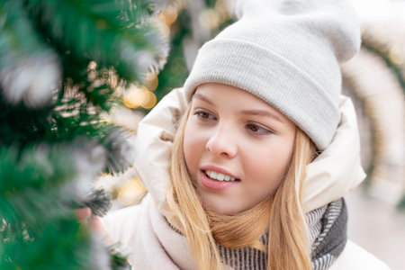 portrait of a teenage girl in winter warm clothes posing near christmas lights