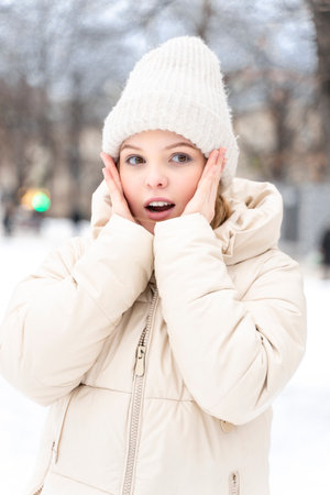 portrait of a teenage girl in winter warm clothes. the woman is surprised, her mouth is open, her hands are on her faceの写真素材