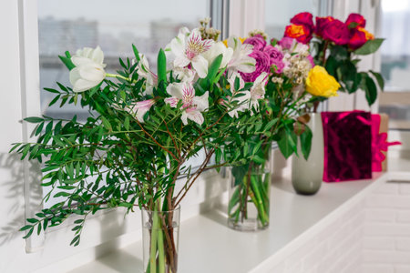 there are vases with different bouquets of flowers and a gift bag on the window. holidays and gifts conceptの写真素材