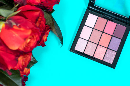 decorative composition with cosmetics and flowers. roses and eyeshadow on blue backgroundの写真素材