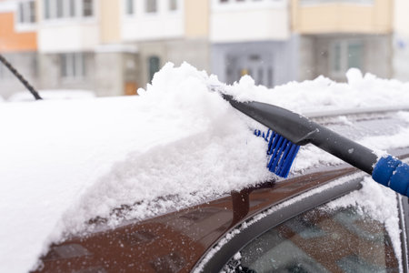 the driver cleans snow from the roof of the car with a brushの写真素材