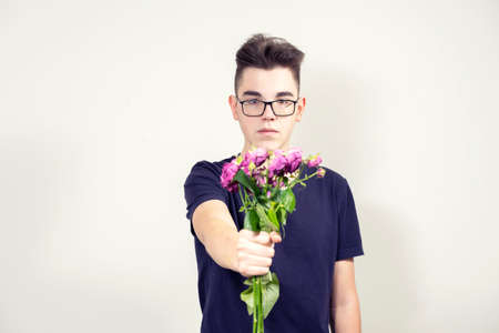 a serious young man in glasses holds out a bouquet of not fresh flowers. separation conceptの写真素材