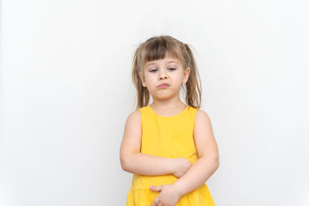 portrait of a displeased naughty little girl in a yellow dress on a gray backgroundの写真素材