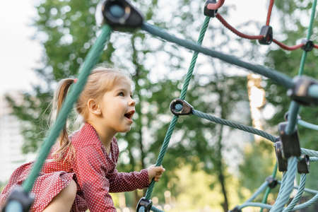 Children play and climb outdoors on a sunny summer day. Nice kid girl on a swing nest in a preschool sports complex.の写真素材