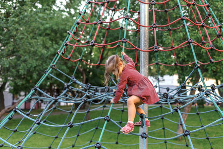 little girl in red dress playing on the playground on a summer day. Healthy summer activity for...