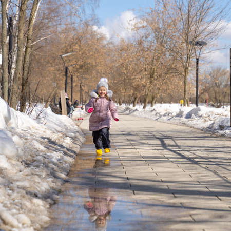 happy little caucasian girl in yellow rubber boots runing in the spring puddles and laughingの写真素材
