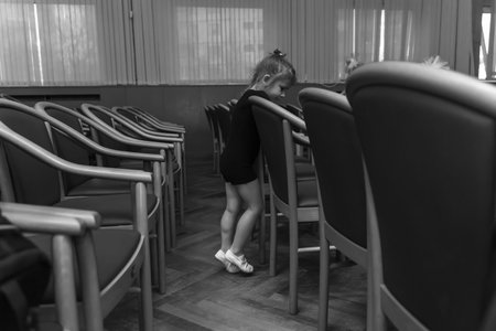 a little girl in a black gymnastic suit and white toe shoes stands alone in an empty auditorium. black and white photoの写真素材