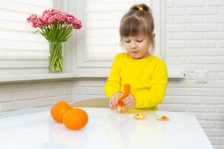 Girl peeling fresh tangerines at table in kitchen, closeup.の写真素材