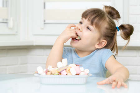 cute European female child smiling, happily eating candy, with appetite. sugar abuse, unhealthy sweet food concept, child candy addiction and child dental careの写真素材