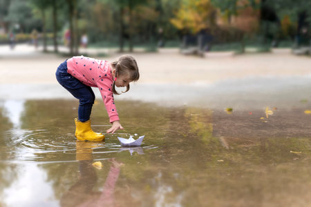 little girl playing with paper boats in puddle