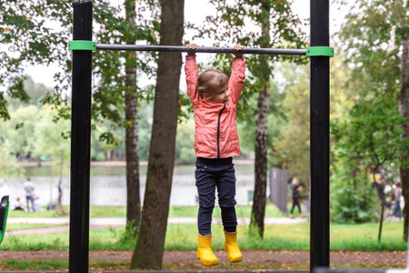 a little girl hangs on a horizontal bar in an autumn parkの写真素材