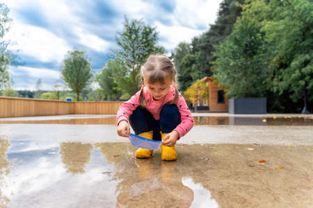 little girl playing with paper boats in puddleの写真素材