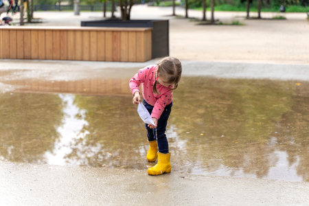 happy child girl with paper boat in a puddle in autumn on natureの写真素材