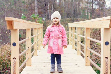 happy little girl stands on a wooden bridge of a forest lake on an autumn dayの写真素材
