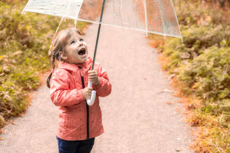 happy child girl with umbrella in a puddle on an autumn walk. little girl opening her mouth looking at water dropletsの写真素材
