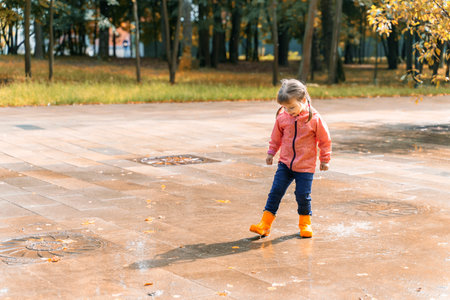 child girl jumping and playing in a puddle after rainの写真素材