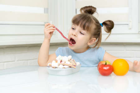 little girl makes a choice between candy and fruit. the child rejects healthy foods and chooses unhealthy foodsの写真素材