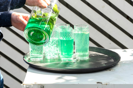 a man pours mojito with mint from a decanter into glasses. street party