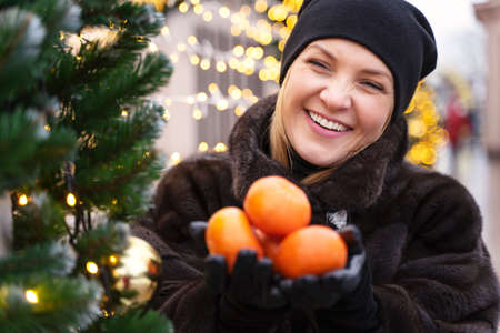 Young woman holding mandarin near a Christmas tree. New year, holiday, health conceptの写真素材