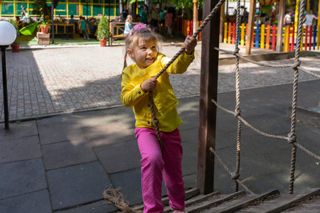 little girl in a yellow jacket and pink pants on the playground.の写真素材