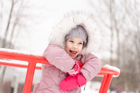 playful child girl in pink coat having fun in winter parkの写真素材