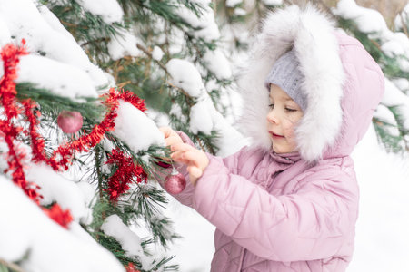 cute baby girl decorate christmas tree outdoorの写真素材