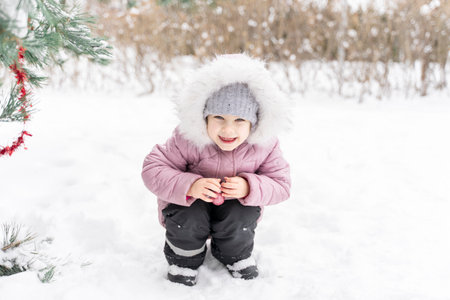 portrait of a cute little girl with a Christmas ball in a fur hood in a snowy winterの写真素材