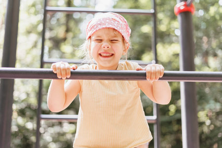 little girl pulls herself up on a horizontal bar in a city park on a summer day